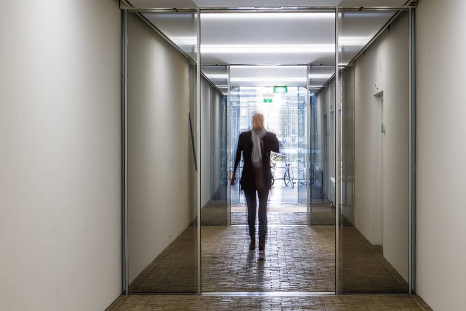 Een medewerker passeert de glazen schuifdeuren van de ingang van het Buitenhof-kantoor.